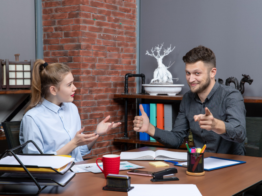 Two colleagues discussing work in a modern office setting with files and stationery on the table — bet immigration lawyer.