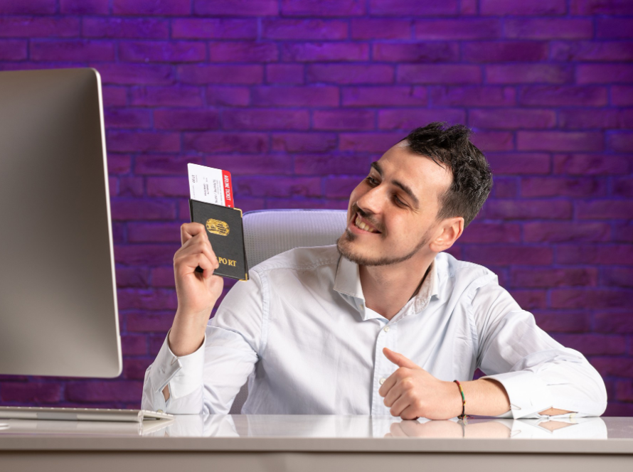 Man smiling at his desk holding a passport and flight tickets, representing O-1 visa approval.