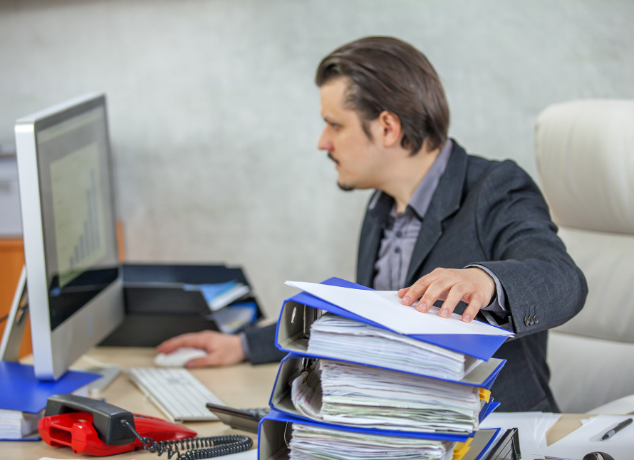 Man working at a desk with a large stack of paperwork.