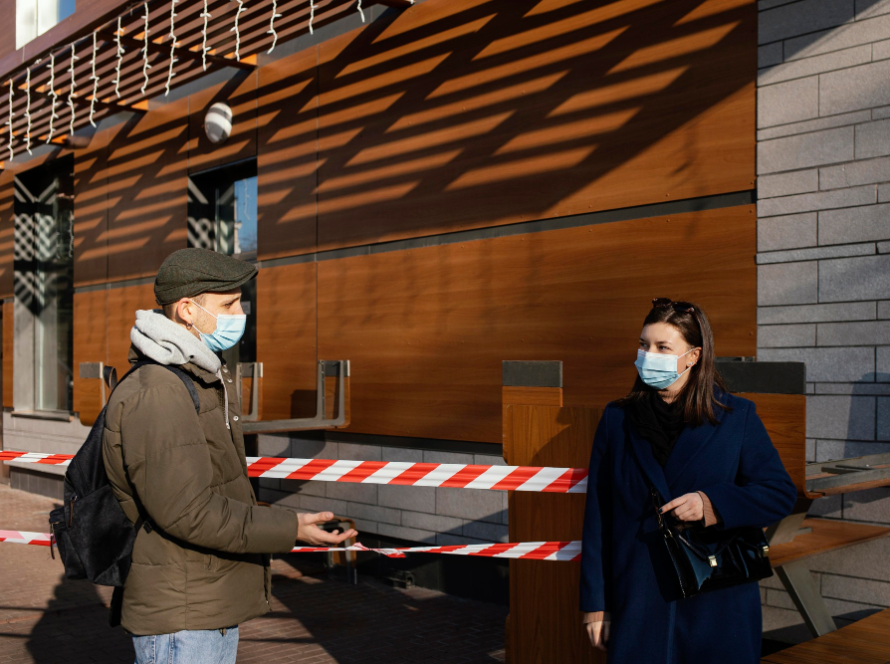 A man and a woman wearing masks stand near a red and white caution tape in front of a building.