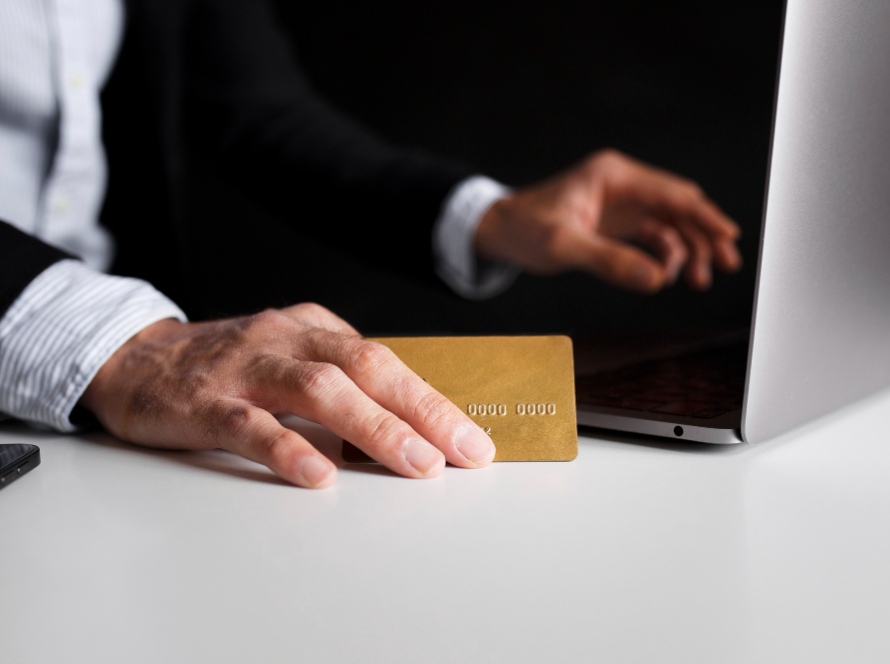 Trump Gold Card / Gold Visa Explained: What It Is and Who Can Qualify – close-up of a person holding a gold card while using a laptop, symbolizing premium visa or investment-based immigration.